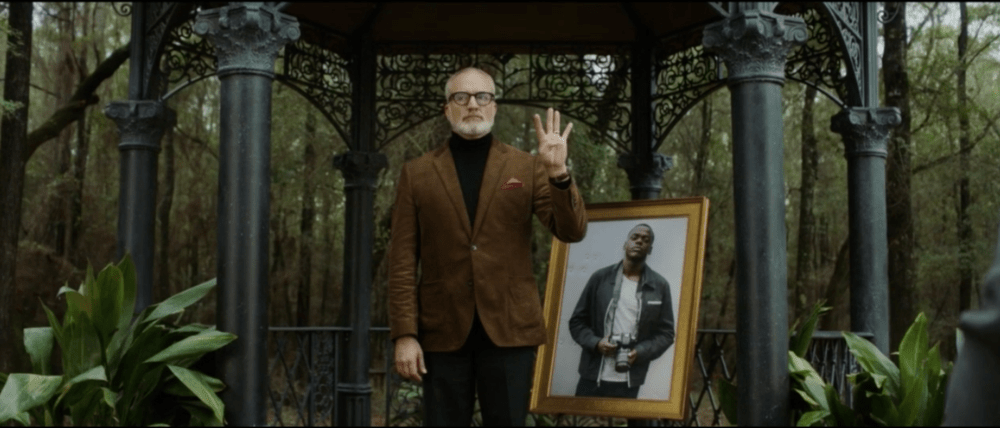 man holds up four fingers as he stands in front of a portrait 