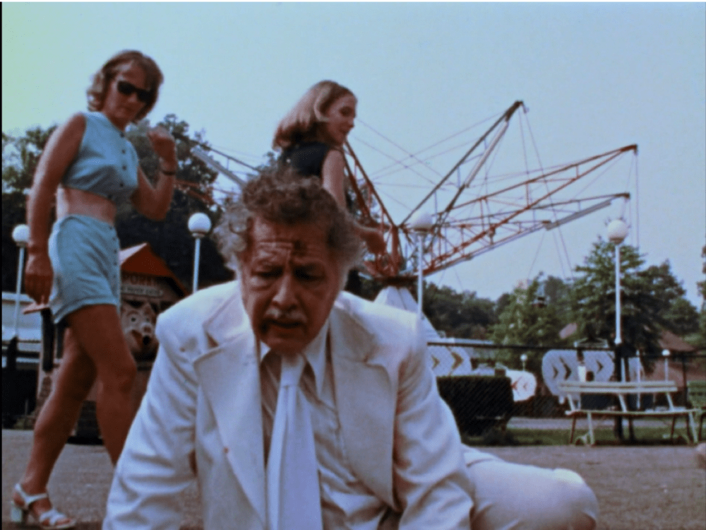 man in a white suit on the ground while two women walk by him