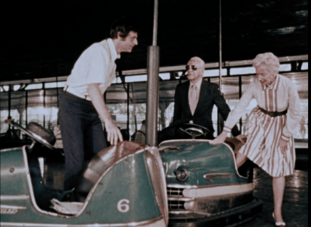 elderly couple in a bumper car next to a middle aged man in a bumper car