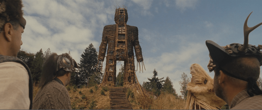 people gaze at a large, robot like structure made of earth materials