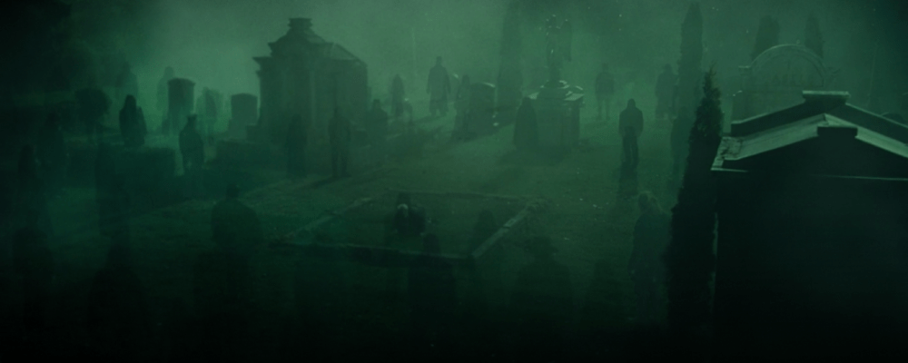 figures stand in a graveyard obscured by a green mist