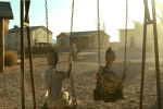 two dolls sit on swings in the middle of a desolate town