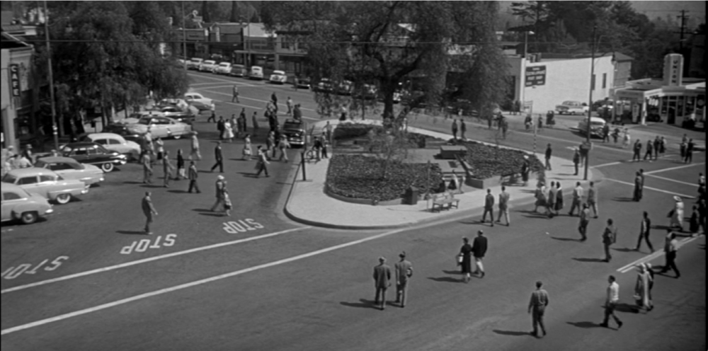 a black and white image of people walking in a town square