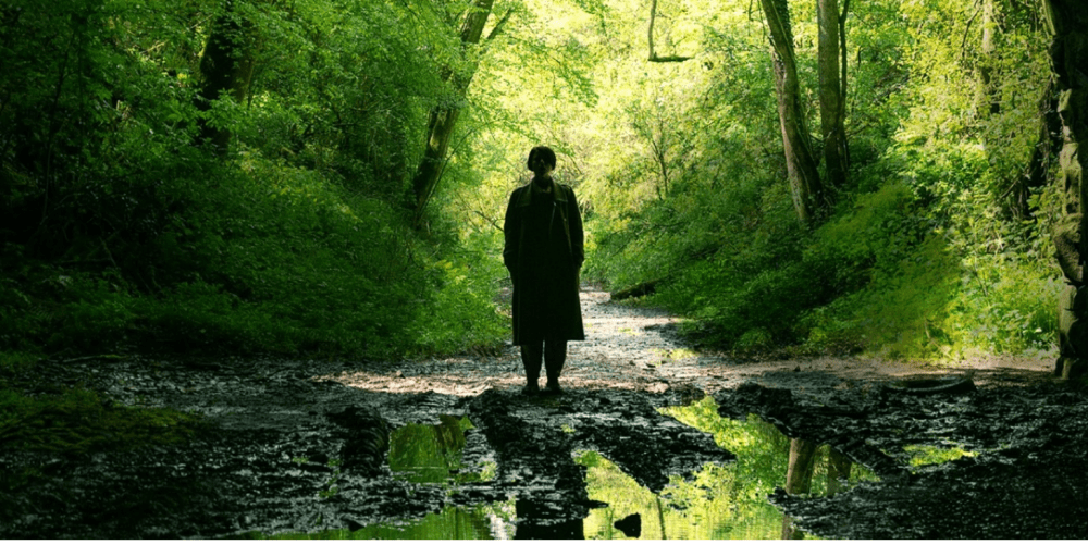 woman stands in a lush, green forest